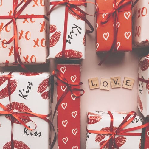 a photo of gifts wrapped in valentines day paper and scrabble tiles laid out that spell LOVE