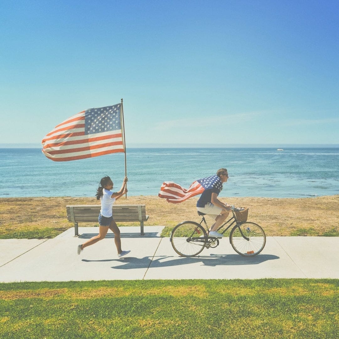 a man riding a bike and a women running behind him with an American flag