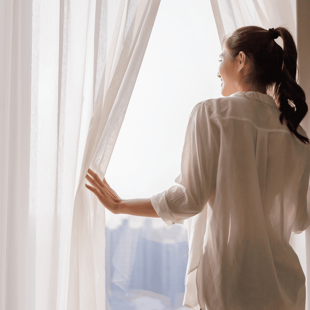 a women opening curtains to look out the window